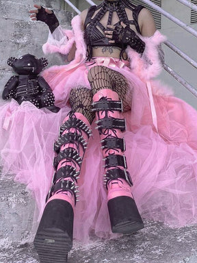 A model sits on steps in the pink layered tutu skirt, with the long mesh panels spread beside heavy black boots.