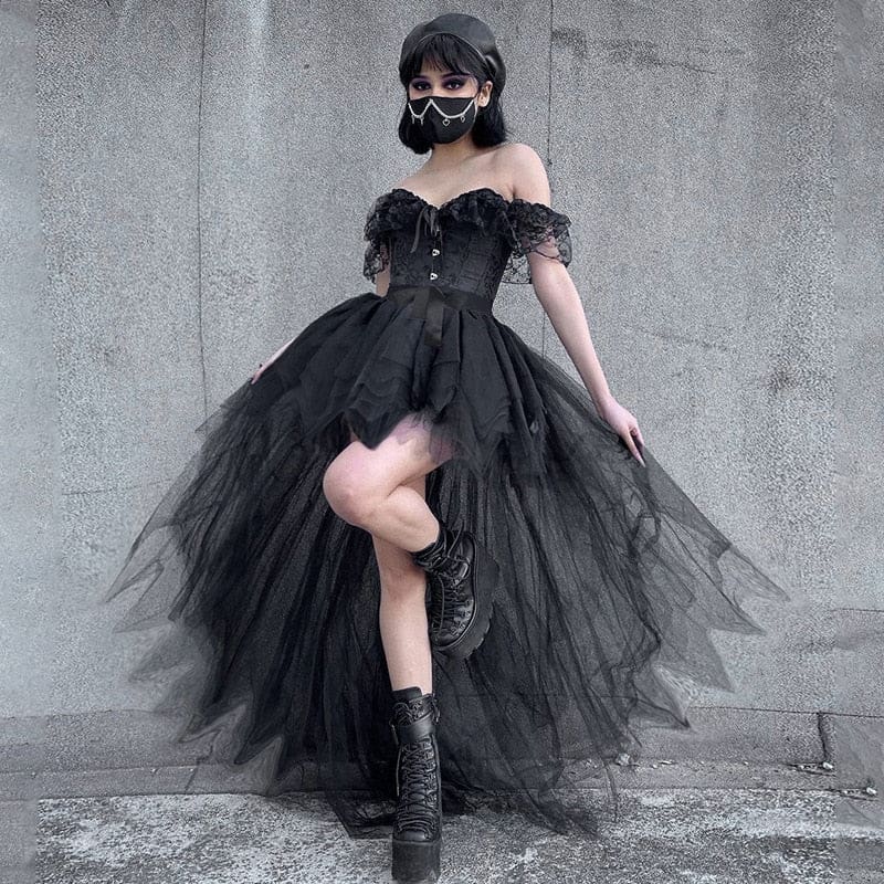 Full outfit view of the black pointed-hem tutu skirt with one leg raised, a fitted black top and patterned tights against a pale wall.