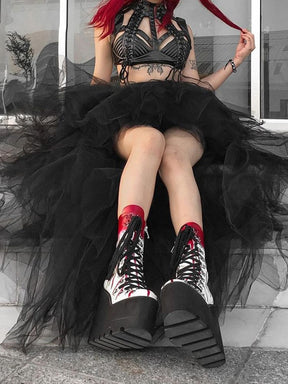 A red-haired model sits on steps wearing the black mesh tutu skirt, with bent knees lifting the short front layers above patterned tights.