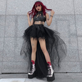A red-haired model stands against a gray wall in the black high-low mesh skirt, with tall boots beneath its layered points.