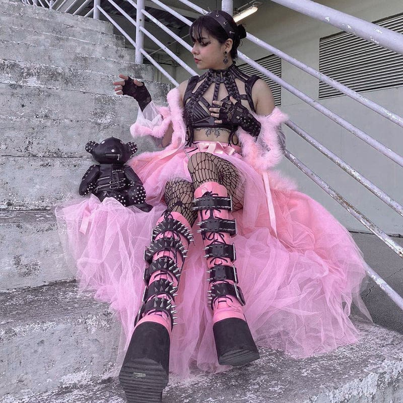 Wider view of the pink tutu skirt spread over outdoor steps around a seated model wearing tall black boots.