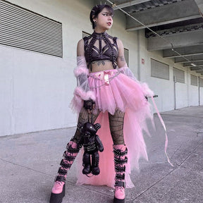 Front outfit view of the pink high-low skirt, showing its ribbon waist bow above patterned hosiery and a black bag.