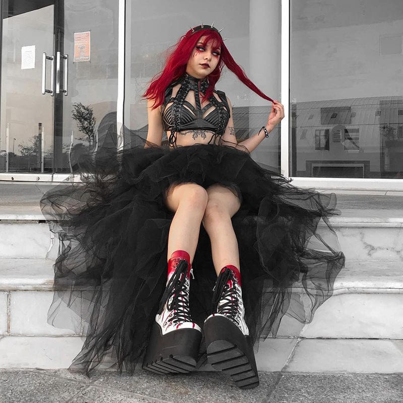 The black tutu skirt drapes over steps around a seated red-haired model, showing its longer panels to either side of the boots.