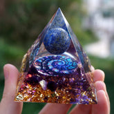 Fibonacci-inspired lapis lazuli orgone pyramid with a blue sphere, spiral inlay and purple amethyst layers. Close front view held outdoors with gold-tone flecks visible below the spiral.