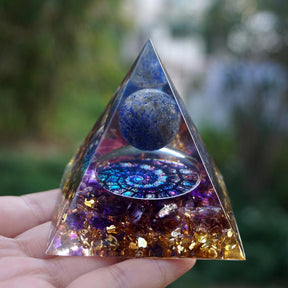 Fibonacci-inspired lapis lazuli orgone pyramid with a blue sphere, spiral inlay and purple amethyst layers. Upright palm view with the blue sphere, copper-coloured outline and purple lower layer.