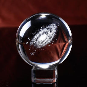 Galaxy crystal ball resting on a transparent square base, showing the spiral design through the rounded side.