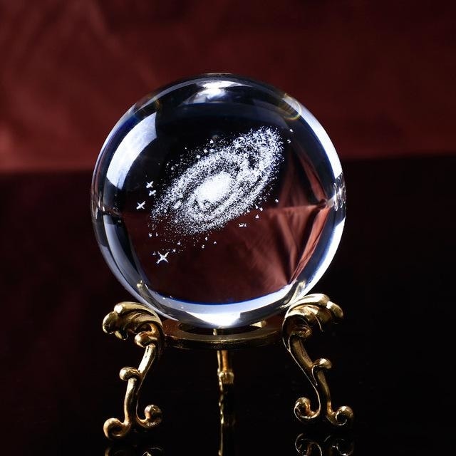 Angled view of the clear galaxy sphere on a gold-tone stand with curling decorative legs.