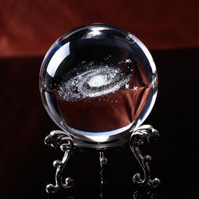 Clear galaxy crystal ball on an ornate silver-tone stand, with a spiral of white stars visible inside the sphere.