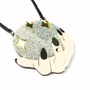 Angled detail of the flat acrylic crystal-ball pendant, showing the glittering silver centre, reflective gold stars and illustrated hands with celestial markings.