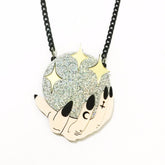 Acrylic pendant necklace depicting pale hands with black nails around a silver glitter crystal ball dotted with gold stars, suspended from a black chain on white.