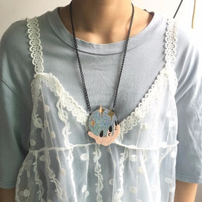 A model wears the crystal-ball hands necklace over a grey top and a light dotted slip layer, showing the black chain and glittering pendant against the neckline.