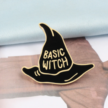 Gold-tone Basic Witch hat pin displayed on printed paper, with bold lettering against black enamel.