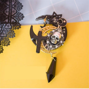 Steampunk skull hair clip arranged on yellow beside black lace. Layered crescent moons, star details and the long faceted drop contrast with the bright background.