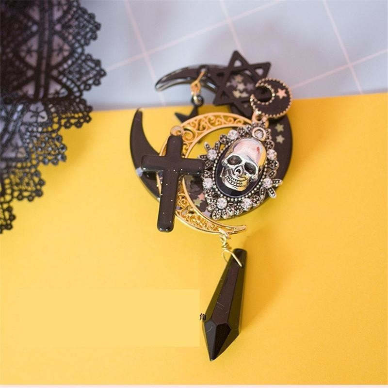 Steampunk skull hair clip arranged on yellow beside black lace. Layered crescent moons, star details and the long faceted drop contrast with the bright background.