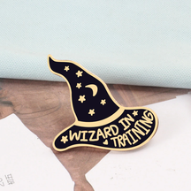 Gold-tone Wizard in Training pin on printed paper, with purple enamel, small stars and a crescent moon.
