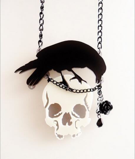 Angled suspended view of the gothic crow-and-skull necklace, showing the layered pendant outline and asymmetric rose-and-drop detail.
