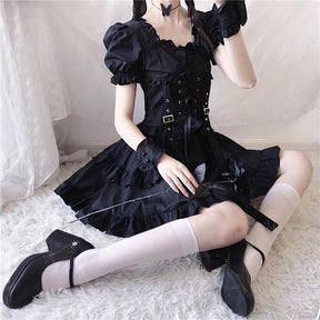 Alternate copy of the seated black dress view, with white stockings, black shoes and the layered hem visible.
