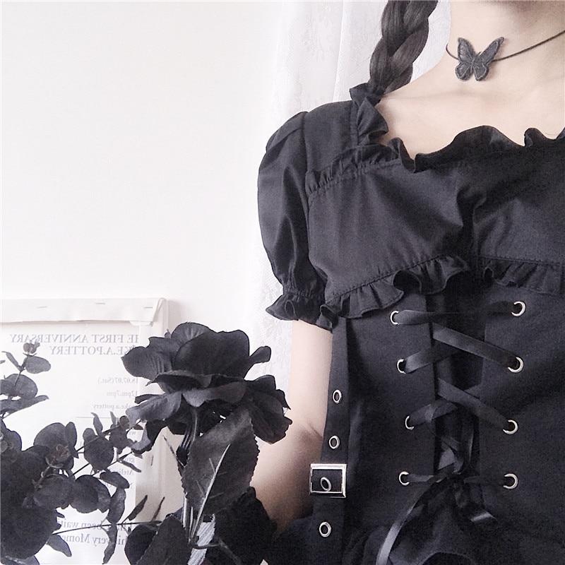 Close-up of the black dress neckline and puff sleeve beside the corset harness, showing the frilled edge, eyelets and crossing ribbon.