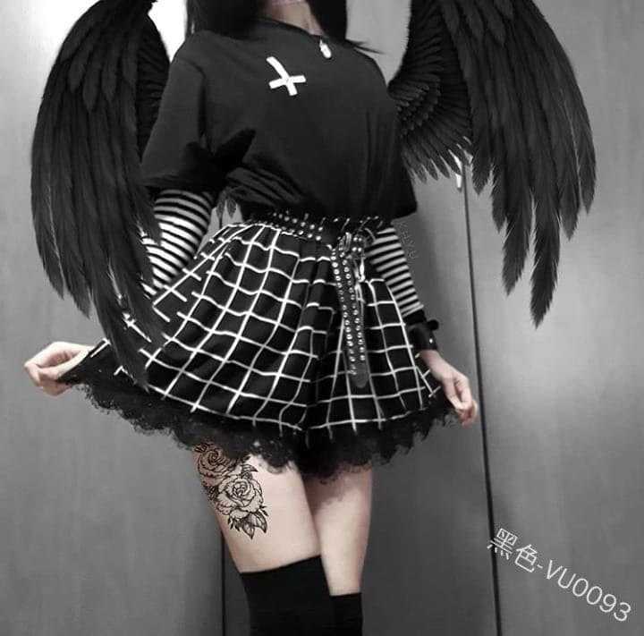 Fuller front view of the black-and-white grid skort, styled with a dark top and belt. The angled white lines follow the folds above a soft black lace edge.
