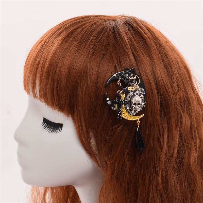Black and gold-tone skull moon clip worn at the side of an auburn wig on a mannequin. The ornate cameo sits above the dangling black faceted charm.