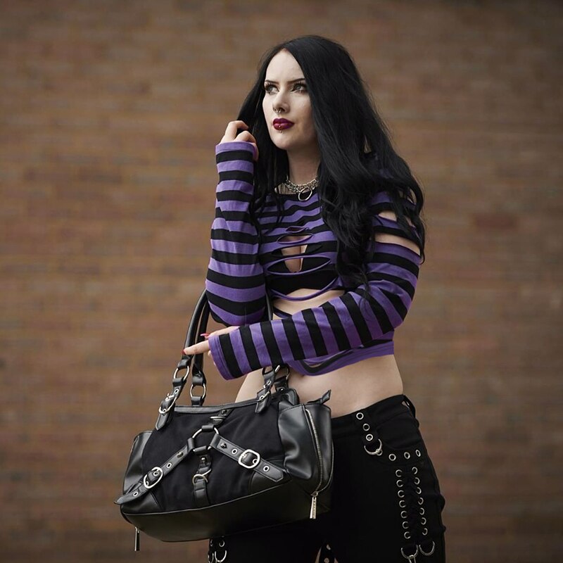 Purple striped crop sweater worn with black trousers and a buckle handbag, with one long sleeve raised beside the face.