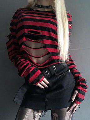 Red and black striped crop sweater with a slashed front, worn with a black mini skirt and wide eyelet belt against a gray wall.