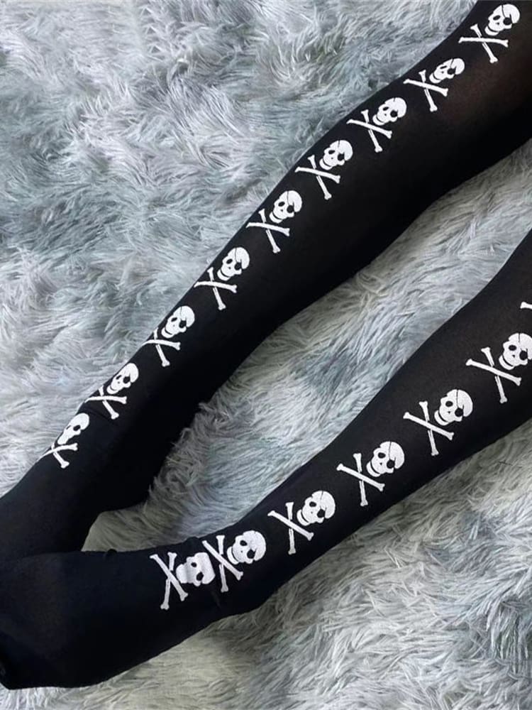 Diagonal view of black thigh-high stockings with white skull-and-crossbones lines over a grey rug.