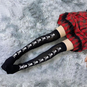Black skull-line thigh-high stockings styled below a red plaid hem over a grey rug.