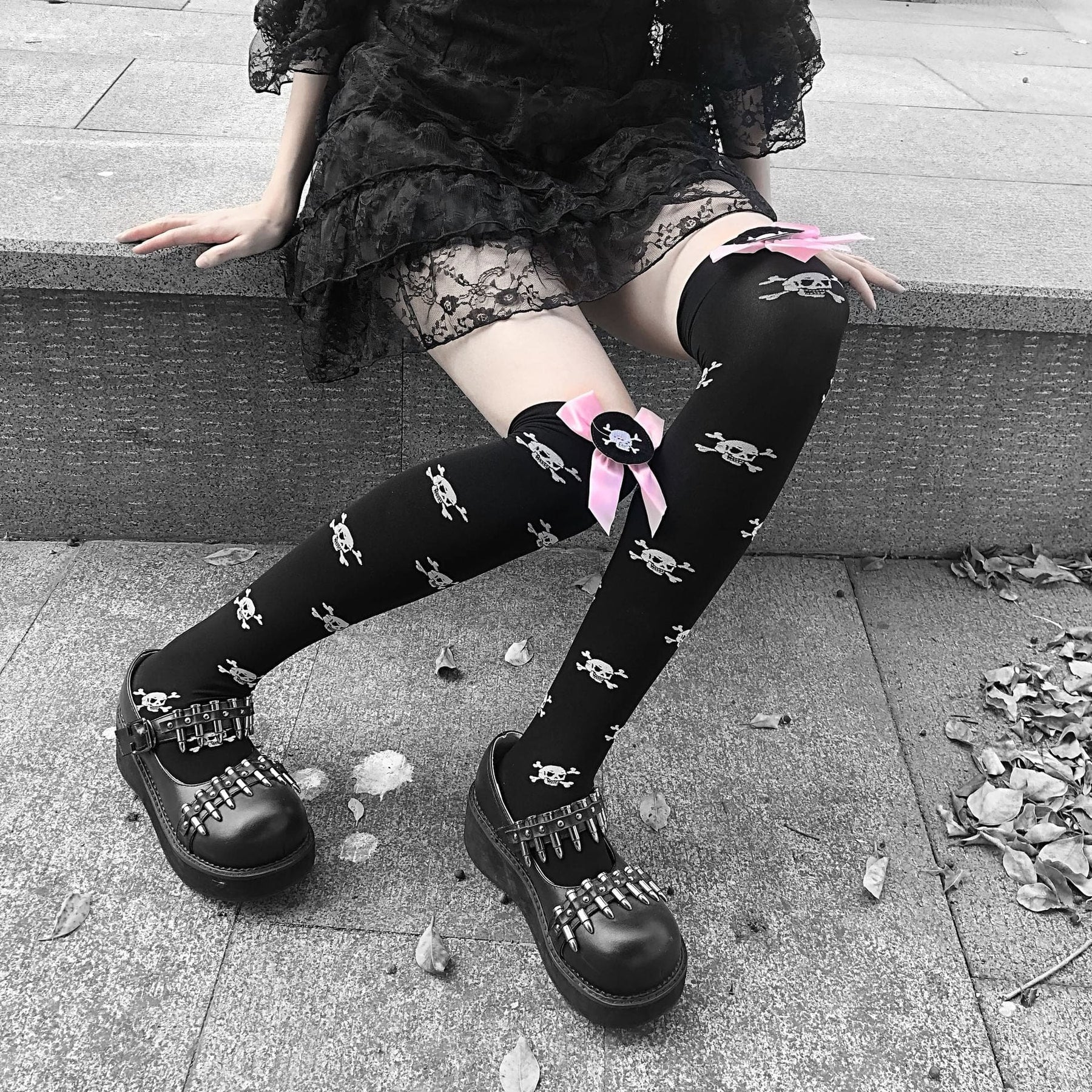 Square view of black skull-print stockings with pink bows, shown with the legs angled from a ledge.