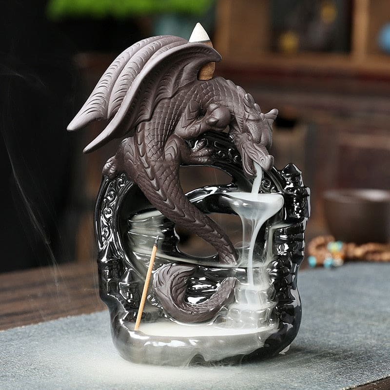 Front three-quarter view of the dragon backflow burner on a tabletop, with a cone above the wings and smoke cascading from the mouth to the base.