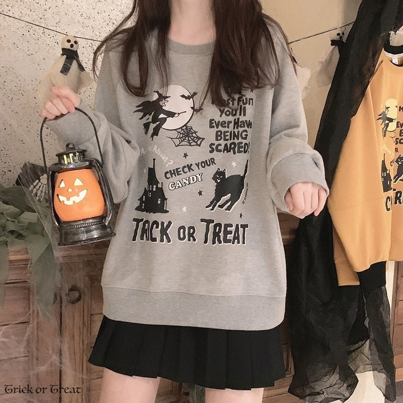 Gray Halloween crewneck sweatshirt worn with a black skirt while holding a pumpkin lantern, showing the large black Trick or Treat illustration.
