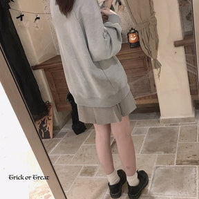 Rear mirror view of the gray crewneck sweatshirt, showing the plain back and relaxed fit above a short skirt and black shoes.