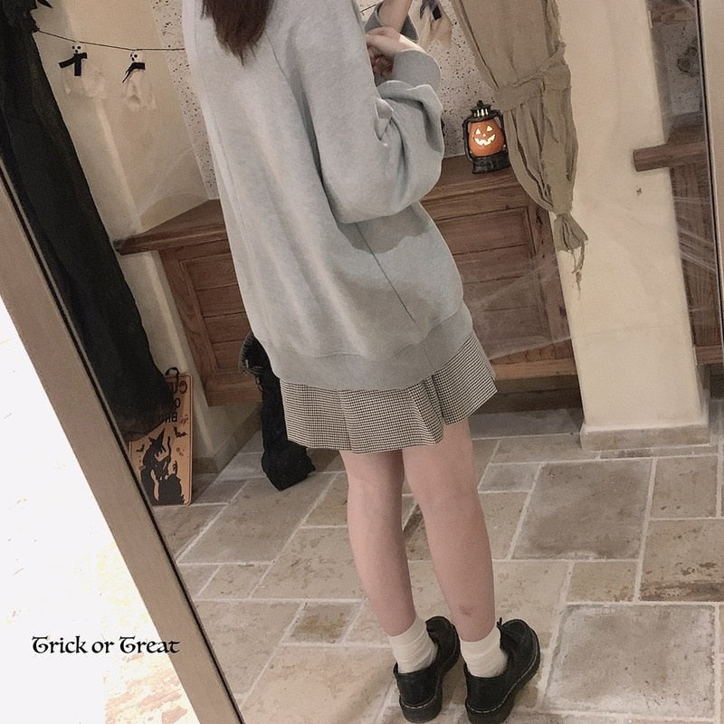 Rear mirror view of the gray crewneck sweatshirt, showing the plain back and relaxed fit above a short skirt and black shoes.