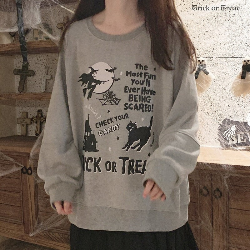 Gray Trick or Treat sweatshirt photographed from the front, with its black cat, castle and flying witch artwork visible against the pale gray body.