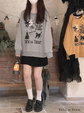 Full outfit view of the gray Halloween sweatshirt with a short black skirt, white socks and black shoes, with a pumpkin lantern held at one side.
