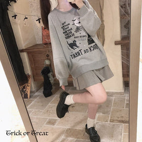 Gray Trick or Treat sweatshirt worn with a short pleated skirt in a mirror pose with one leg lifted, showing its loose body and sleeves.