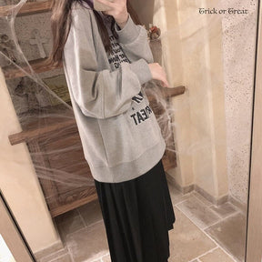 Side mirror view of the gray Halloween sweatshirt above a long black pleated skirt, showing the dropped shoulder and ribbed hem.