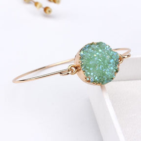 Green druzy quartz circle cuff angled on a white block, showing the raised sparkling face above its slender gold-tone band.