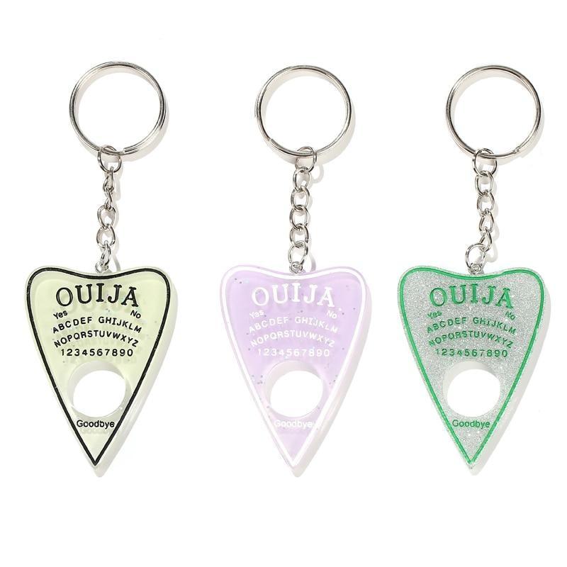 Three planchette keychains displayed on white: pale green with black lettering, lavender with white lettering and silver glitter with green lettering.