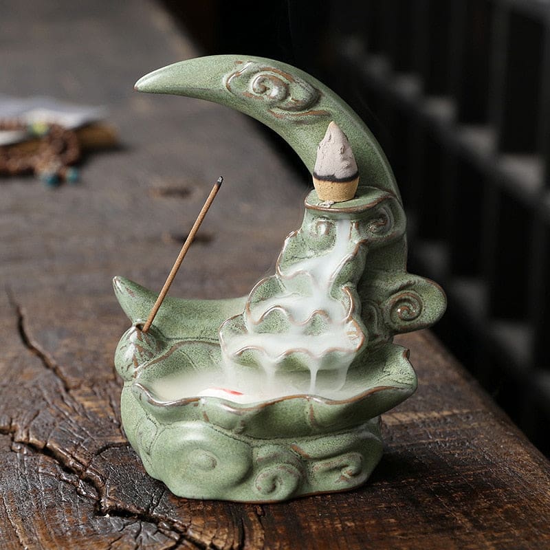 Green crescent moon burner on a wooden surface, with an incense stick beside the sculpted waterfall path and a cone resting near the upper curve.