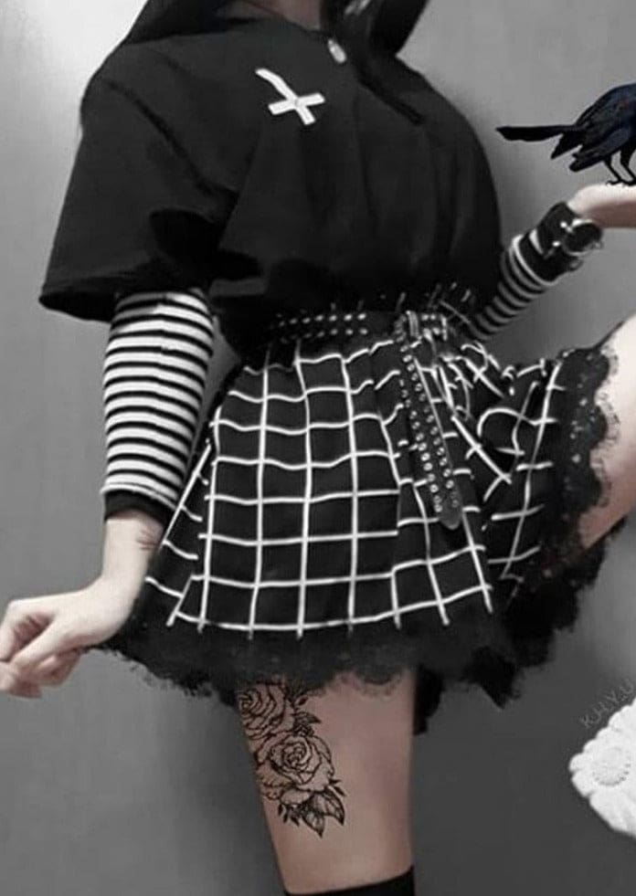 Close view of the grid-print skort with one leg raised, showing the flared panels and scalloped black lace trim against the thighs.
