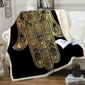 Black and gold hamsa throw blanket draped over a chair with its pale sherpa reverse visible.