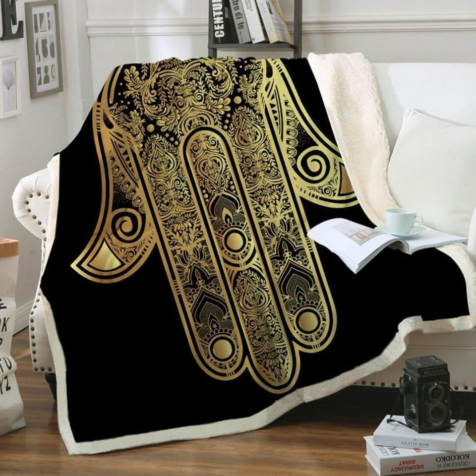 Black and gold hamsa throw blanket draped over a chair with its pale sherpa reverse visible.