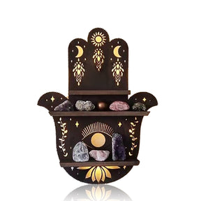 Hamsa hand-shaped wooden shelf against white, showing three ledges styled with small stones beneath sun, moon and eye motifs.