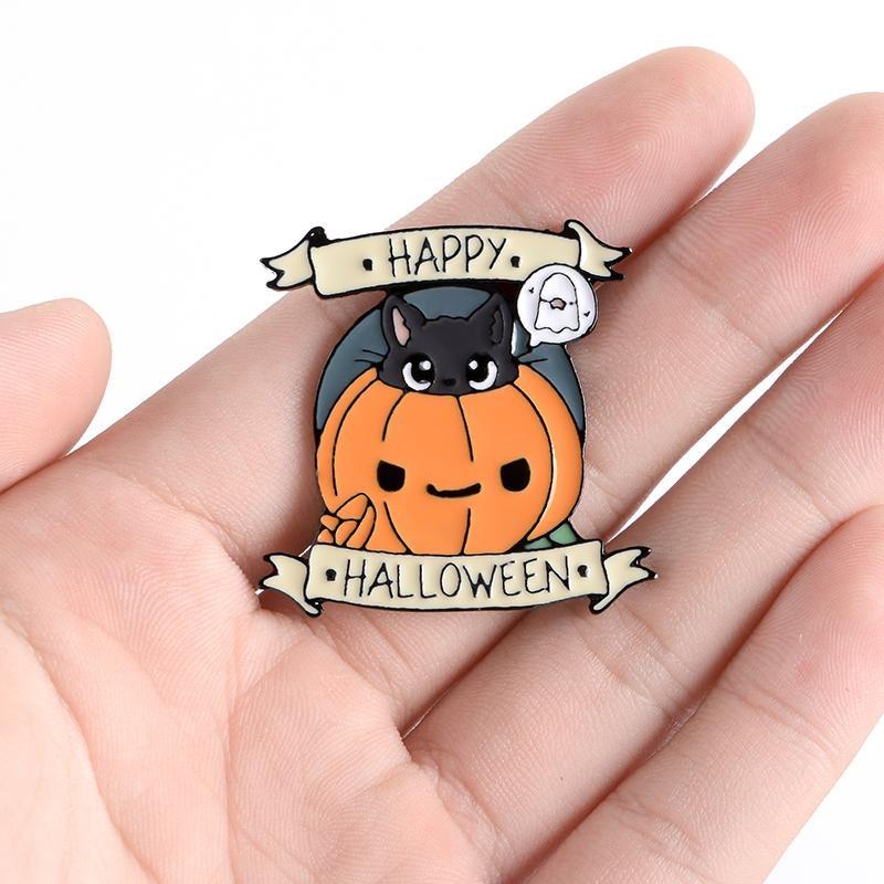 Black cat and pumpkin Happy Halloween pin resting in an open hand, showing the orange face, tiny ghost and banner lettering.