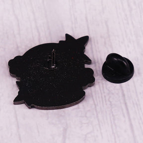 Black reverse of the haunted snowglobe enamel pin with a single upright pin post and detached black rubber clutch on a pale wood surface.