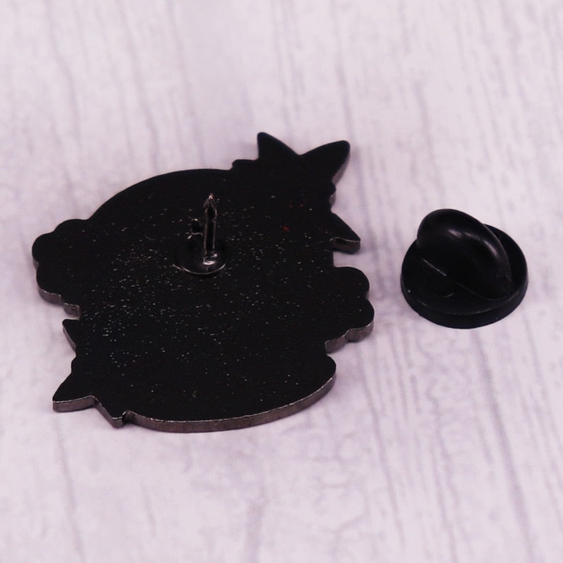 Black reverse of the haunted snowglobe enamel pin with a single upright pin post and detached black rubber clutch on a pale wood surface.