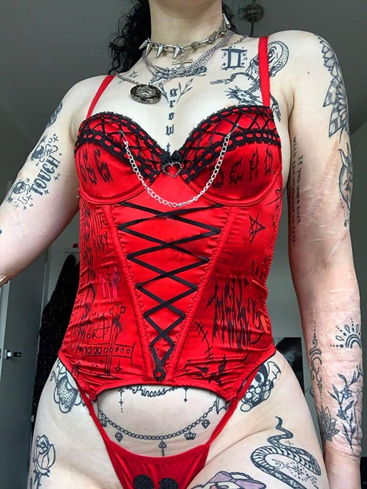 A model wears the red gothic bustier and matching briefs, with black front ribbon lacing, printed symbols and draped silver-tone chains.