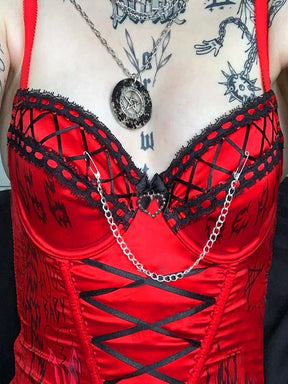 Close-up of the red bustier neckline with black ribbon lattice, lace edging, a central heart and a draped chain.