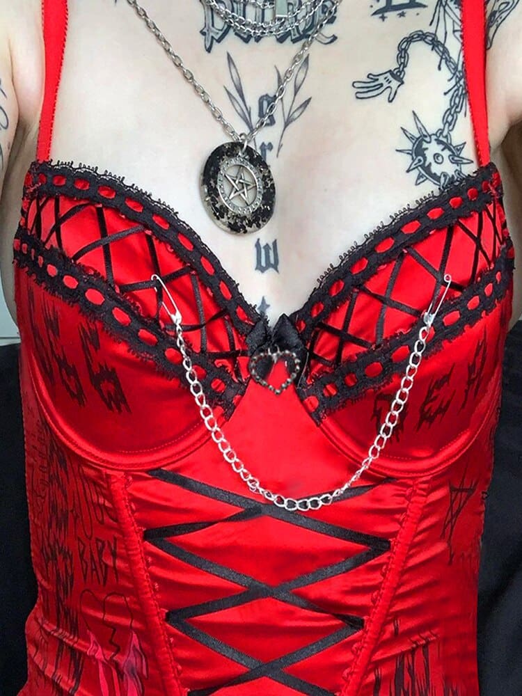 Close-up of the red bustier neckline with black ribbon lattice, lace edging, a central heart and a draped chain.